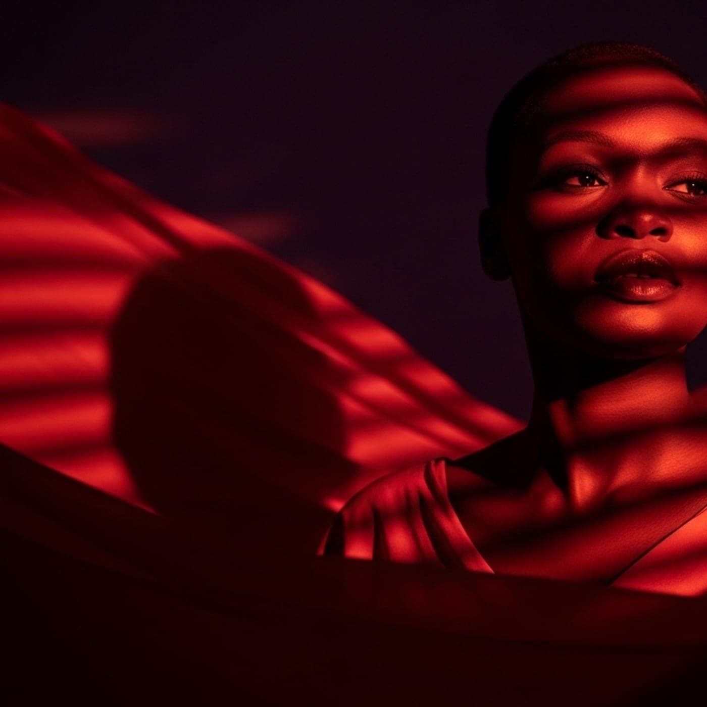 A woman lit in deep red light, turning her face toward something out of frame