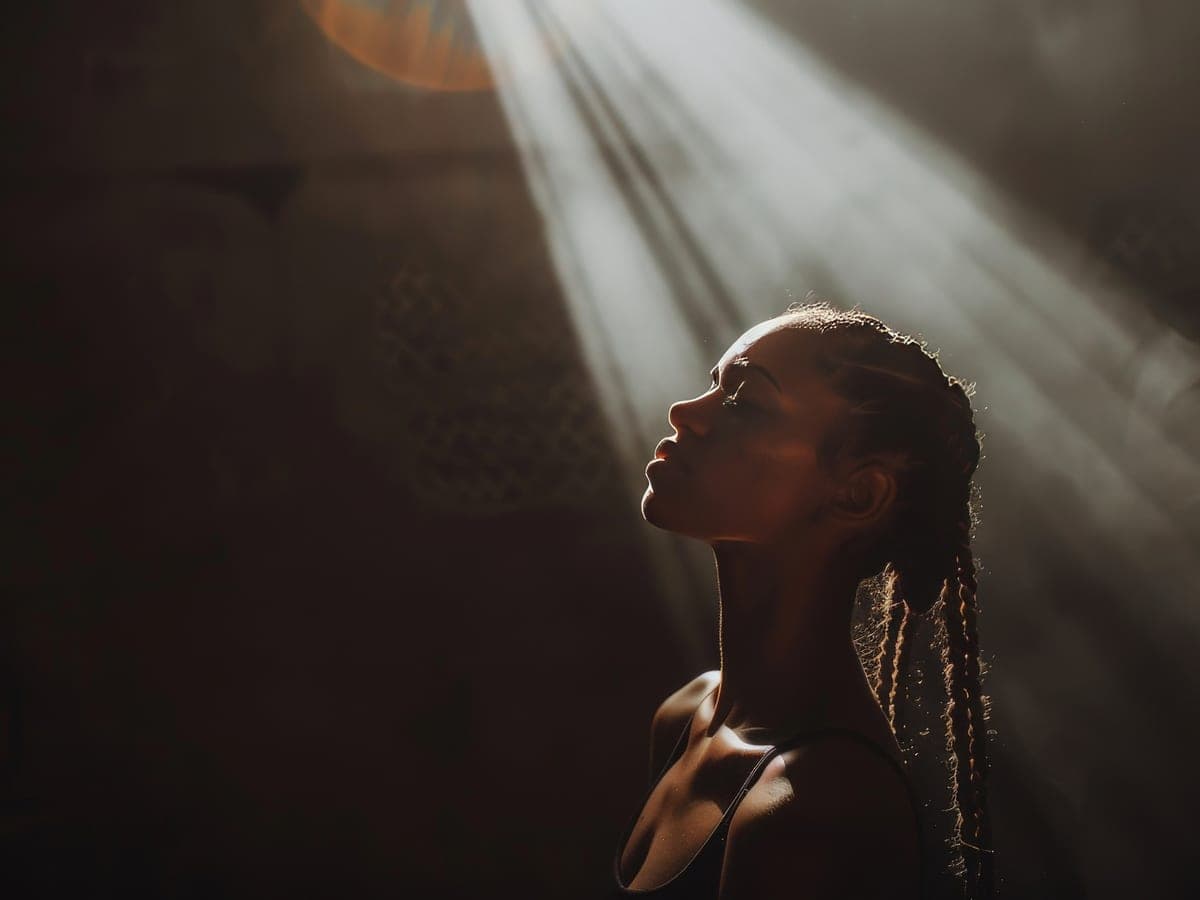 A woman standing inside a shaft of daylight with her face lifted into it